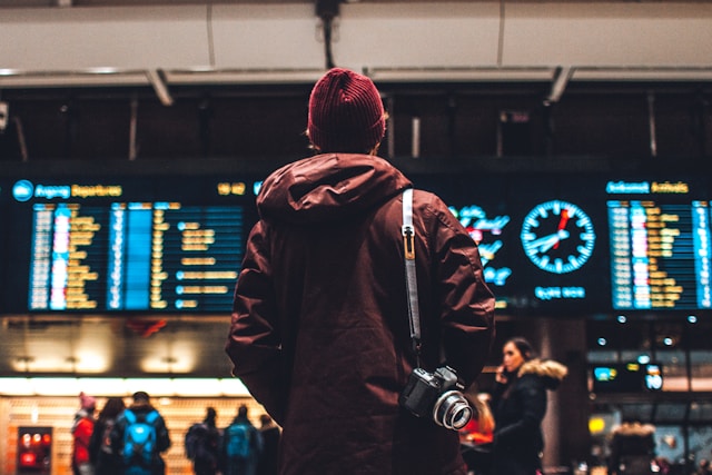a man wearing a hat stands in front of airport departure screens